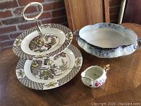 Photo showing assembled Ridgeways tiered server with three decorated porcelain plates, oval blue and white dish, and small creamer on wooden table.
