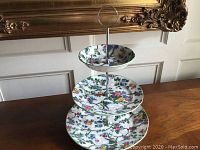 Full view of three-tiered ceramic server showing all three decorated plates stacked with a metal center rod and ring handle