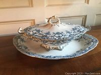 Blue and white ceramic tureen on matching platter showing floral transferware pattern and ornate handle on lid.