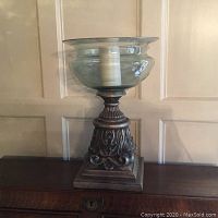 Full view of large candle holder showing glass hurricane shade and ornate carved base on wooden surface.
