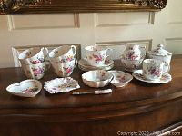 Overview of tea service pieces arranged on table showing cups, saucers, sugar and cream vessels, trinket dishes and spreader