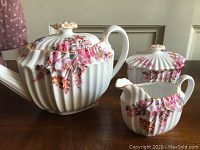 Fluted teapot, sugar bowl with lid and creamer on wood surface