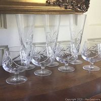 Front view of four brandy snifters and three pilsner glasses with detailed cut patterns on a wooden surface.