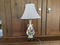 Full view of the Royal Winton lamp on a wooden cabinet, showing the painted ceramic base and beige fabric shade.