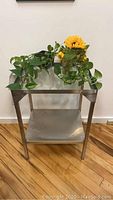 Front view of one stainless steel and glass bar cart showing metal lower shelf and glass top with decorative plants