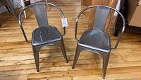 Two metal chairs side by side photographed on a wooden floor.