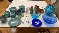 Full lot image showing aqua ceramic plant pots, blue glass bowls, swirled large blue glass vase with lid, silver vases, glass bottles, small wicker basket, green glass dish and blue hanging ornaments.