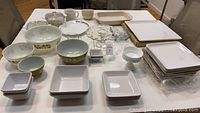 Various kitchen dishes including four Pyrex bowls with olive green floral pattern, Berger baking dish, CorningWare, white square dishes and dinner plates, and a white footed dessert dish.