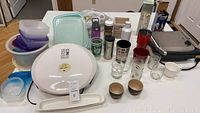 Full lot view showing George Foreman grill, Tupperware containers, assorted glasses, mugs, and metal water bottles on table.