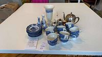 All items displayed on a table including 12 blue and white teacups and saucers, 4 vases, 3 metal teapots.