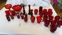 Wide view of entire red glassware lot showing all pieces including cream and sugar set, glasses, candleholders, and bowls.