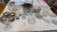 Full overview of the entire lot showing multiple cut glass dishes, etched glass bowls, crystal bowls, and a set of metal bucket containers with glass inserts arranged on a table.