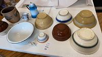 Top view of rustic and primitive bowls and serving items displayed on table, including beige, brown, white bowls, blue miniature pitcher and small decorative cup.