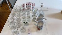 Full set on white table showing ceramic lobster butter melters, glass decanter with stopper, various clear stemmed glasses, frosted glasses, and tall lobster glasses.