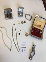 Overview of two jewelry boxes, bracelets, necklaces, rings, cufflinks, pins and one wristwatch on white background with lot tag