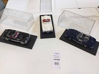Three Corvette model cars placed on a table with their clear display cases open or removed, showing white, black, and dark blue models.