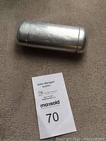 Silver-tone metal cigarette case with intricate engraved designs on the surface shown from above on a dark fabric.