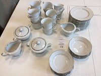 Full set of white china dinnerware arranged on table showing cups, bowls, plates, sugar bowl with lid, creamers, and serving bowls all with silver decorative rims.