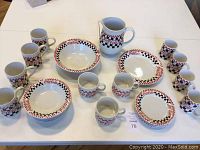 Full set of Coca-Cola branded dinnerware and mugs laid out on a white table. Includes mugs, bowls, plates, and the pitcher.