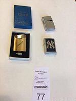 Set of three cigarette lighters including a gold-toned lighter with inscription, a silver lighter with NY Yankees logo, and a plain silver lighter, all on a white background.