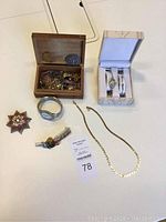 Overall view of jewelry items displayed on table including watches, bracelets, chain necklace, decorative pin, and wooden jewelry box with assorted pieces.
