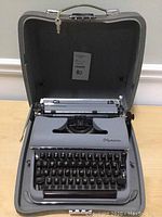 Closed case opened to show the Olympia manual typewriter inside, gray metal body and integrated case interior.