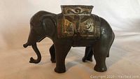 Side view of vintage cast iron elephant coin bank, showing detailed saddle and trunk position.