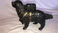 Side view of a black cast iron dog coin bank with gold painted straps and saddlebag detail