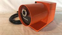 Angled front view of orange Panasonic electric pencil sharpener showing cylindrical pencil insertion labeled Panasonic, power cord visible.