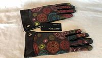 Top view of gloves showing colorful decorative circular pattern on one leather glove and solid black leather on the other glove's fingers and wrist area