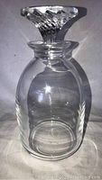 Front view of Lalique crystal decanter with stopper, showing smooth rounded body and decorative stopper.