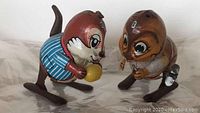Front view of two vintage clockwork tin toys showing cat with blue outfit and dog with red scarf facing forward