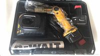 Open carrying case containing DeWalt cordless screwdriver wrapped in plastic, charger, two batteries, and paperwork arranged inside.