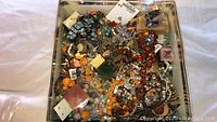 Wide view of box filled with assorted costume jewelry including beads, chains, and pendants