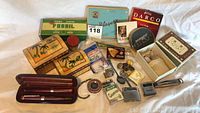 Overview of the lot showing all items including boxes with tropical designs, branded tins, pens in wooden case, various small items.