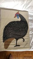 Full view of the bird painting on fabric in a Lucite frame, showing the entire bird with black body and white dots, red and blue head details, and signature at bottom right.
