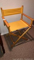 Yellow folding directors chair angled front view, showing fabric seat and backrest with wooden frame and armrests.