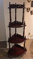 Full view of four-tier wooden corner what not shelf showing turned spindle supports and carved details.