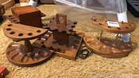 Photo showing three different wooden pipe racks along with a wooden humidor box and a small metal accessory placed on carpeted floor.