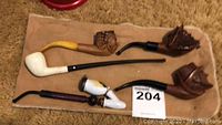 Five varied smoking pipes laid out on cloth, each with distinct styles and materials