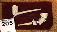 Two decorative carved pipes placed on a velvet cloth with auction tag visible.