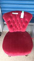 Front view of red velvet slipper chair showing tufted backrest and rounded cushioned seat.