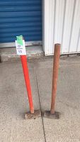 Photo of two sledgehammers standing upright, both with worn wooden handles, one orange painted and one natural wood.