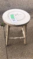 Full view of the distressed white wooden stool showing round seat with distress marks and turned legs.