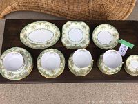 Top-down view of various Noritake pieces including bowls, cups, oval platters, and saucers on wooden table