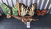 Set of three large wooden butterfly wall hangings and one wooden dinosaur skeleton model placed together for display.