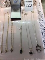 Six necklaces displayed on a surface including gold-tone chains with cross, ring, and crystal pendants plus a silver-tone chain with cameo-style pendant.