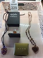 Lot displayed in white tray showing two necklaces and a miniature decorative teapot in display case with branded boxes.