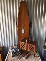 Photo showing vintage wooden ironing board, wooden sewing box, blue woven basket, and knitting needles on a quilted surface
