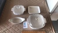 Top view of all 6 bakeware pieces laid out on a quilted surface including two square dishes with glass lids, one square dish without lid, one oval dish with floral print, and one rectangular dish